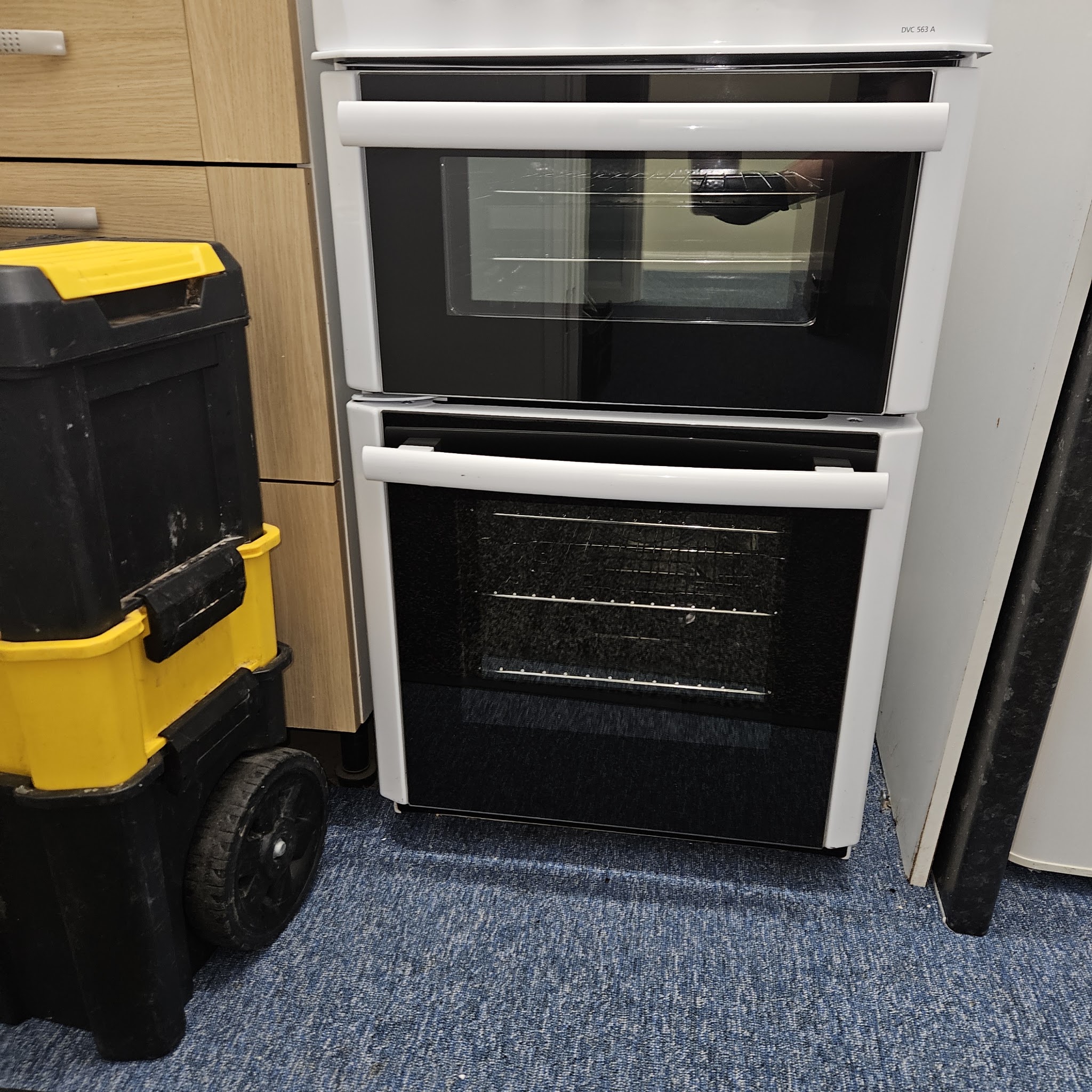 A white freestanding double oven, clean, with a yellow and black tool chest beside it
