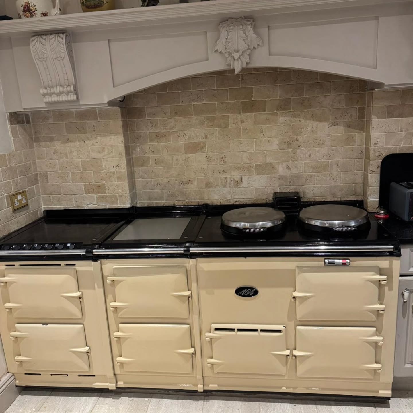 A cream Aga under a stone mantel, cleaned and shining