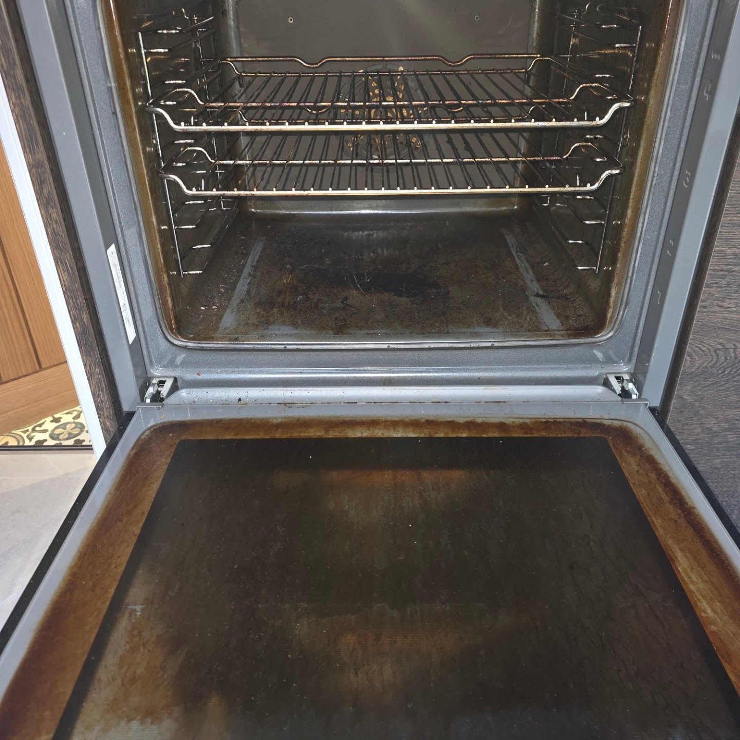 An open oven with a stained, greasy floor and door before cleaning